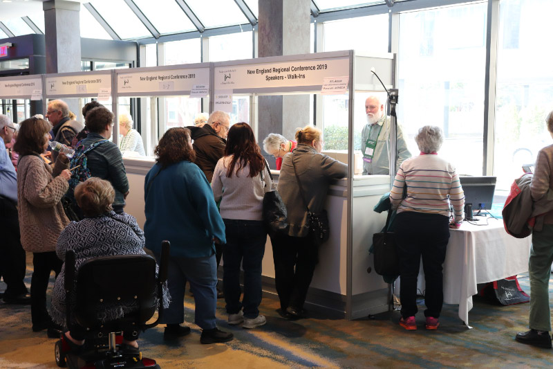 Photo showing 2019 conference attendees picking up their registration packets at the registration desk prior to the start of the conference.